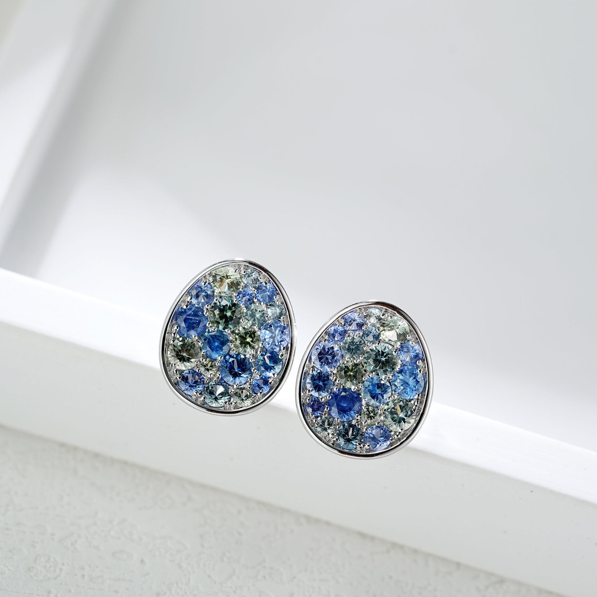 Pair of round earrings with multicolored gemstones on a white surface