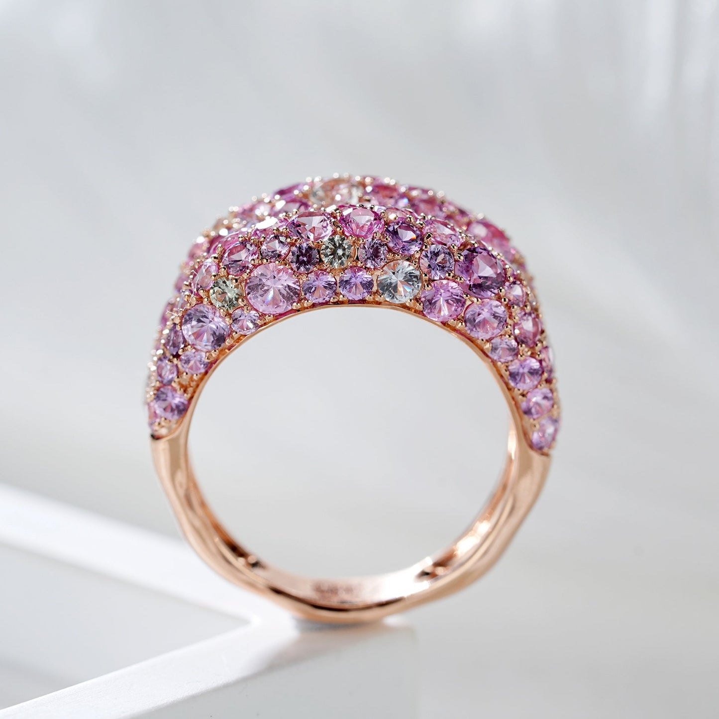 Rose gold ring with pink gemstones on a light gray background