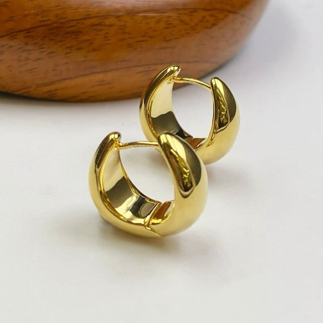Gold hoop earrings on a white surface with a wooden block in the background