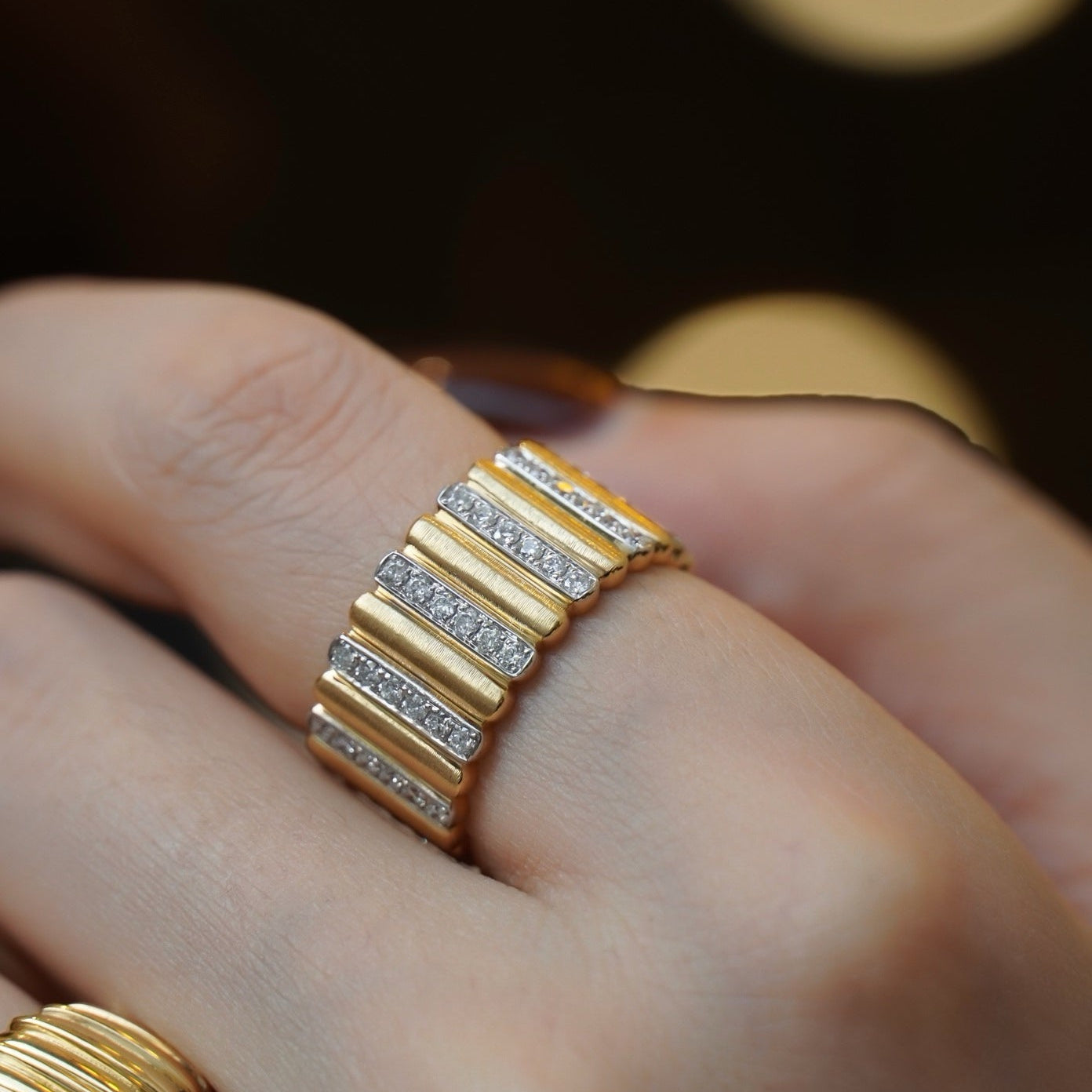 Gold ring with diamond accents on a finger against a dark background