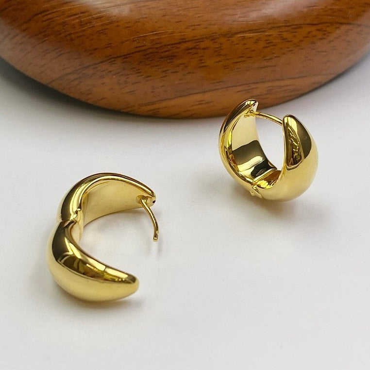 Gold hoop earrings on a white surface with a wooden background